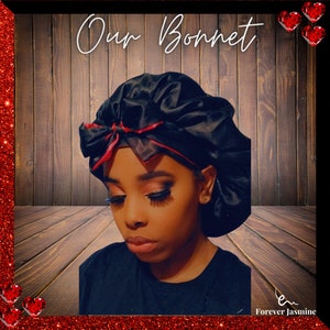 May include: A black satin bonnet with a red trim. The bonnet is worn by a person with dark hair and makeup. The background is a wooden wall with a red glitter border.