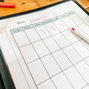 May include: A white dry-erase calendar with the month of March written at the top. The days of the week are listed across the top, and the numbers 1, 2, and 3 are written in red on the calendar.