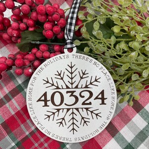 May include: A white round ornament with a snowflake design and the text "Home for the Holidays There's No Place Like Home for the Holidays There's No Place Like" surrounding the number "40324".