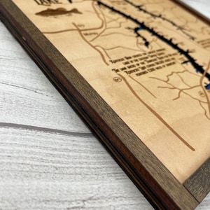 Op de afbeelding: Een houten ingelijste kaart van Kentucky Lake met een donkerbruine lijst en een lichte houten achtergrond. De kaart toont de omtrek van het meer en de omliggende gebieden. De tekst "Kentucky Lake" is zichtbaar bovenaan de kaart.