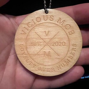 May include: A wooden circle pendant with the text "Vicious Mob" and "Loyalty Over Numbers" around the edge. The center of the circle has a stylized "V" and "M" with the text "Est. 2020" between them.