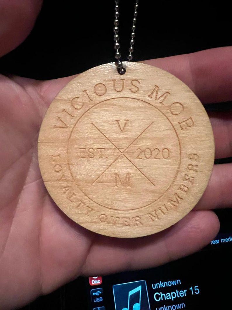May include: A wooden circle pendant with the text "Vicious Mob" and "Loyalty Over Numbers" around the edge. The center of the circle has a stylized "V" and "M" with the text "Est. 2020" between them.