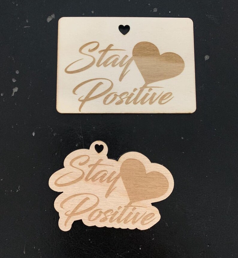 May include: Two wooden ornaments with the text "Stay Positive" and a heart shape. The ornaments are made of light brown wood and have a natural finish.