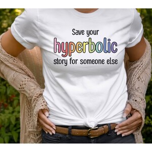 May include: White t-shirt with the text "Save your hyperbolic story for someone else" in black and rainbow colors. The shirt is tied at the waist and worn with a brown belt and jeans.