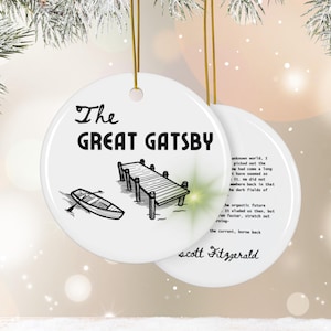 Pu&ograve; includere: Addobbo natalizio in ceramica bianca con un'illustrazione in bianco e nero di un molo e una barca a remi. Il testo "The Great Gatsby" e "Scott Fitzgerald" &egrave; stampato sull'addobbo.