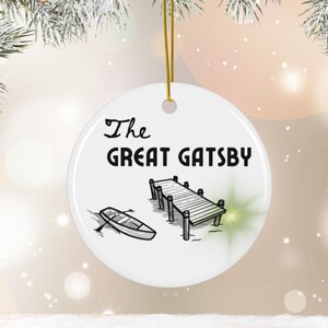 Pu&ograve; includere: Addobbo natalizio in ceramica bianca con un'illustrazione in bianco e nero di un molo e una barca a remi. Il testo "The Great Gatsby" &egrave; stampato in nero sull'addobbo.