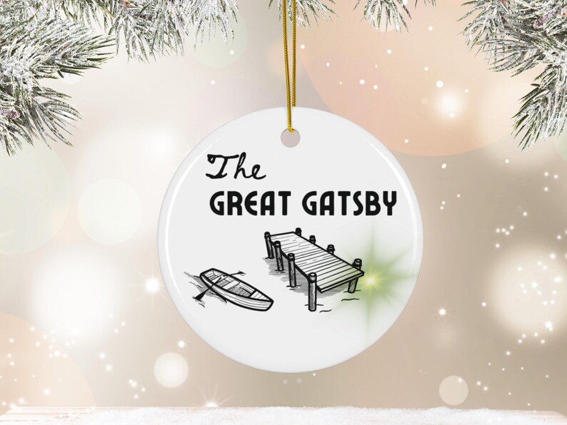 Pu&ograve; includere: Addobbo natalizio in ceramica bianca con un'illustrazione in bianco e nero di un molo e una barca a remi. Il testo "The Great Gatsby" &egrave; stampato in nero sull'addobbo.