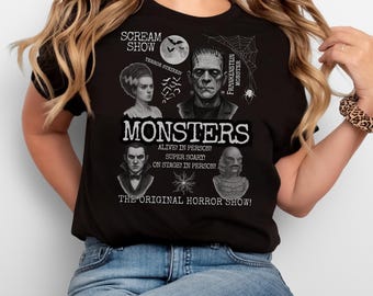 May include: Black t-shirt featuring a graphic design with the word "MONSTERS" and illustrations of classic horror movie characters, including Frankenstein's monster, the Bride of Frankenstein, and the Creature from the Black Lagoon. Text includes "SCREAM SHOW" and "THE ORIGINAL HORROR SHOW!"