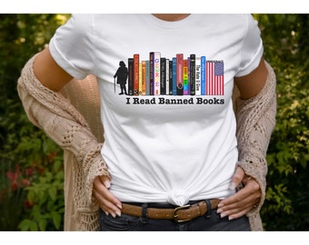 Puede incluir: Camiseta blanca con un diseño de libros, una bandera estadounidense y el texto "I Read Banned Books". El diseño incluye la silueta de una persona con un bastón. Prenda de vestir informal.