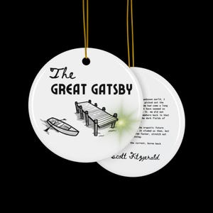Pu&ograve; includere: Ciondolo in ceramica bianca con un'illustrazione in bianco e nero di un molo e una barca. Il testo "The Great Gatsby" &egrave; scritto in lettere nere. Il retro del ciondolo presenta una citazione dal romanzo di F. Scott Fitzgerald.