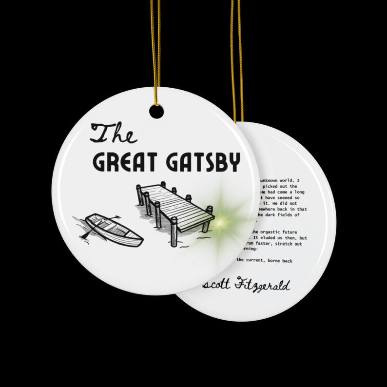 Pu&ograve; includere: Ciondolo in ceramica bianca con un'illustrazione in bianco e nero di un molo e una barca. Il testo "The Great Gatsby" &egrave; scritto in lettere nere. Il retro del ciondolo presenta una citazione dal romanzo di F. Scott Fitzgerald.