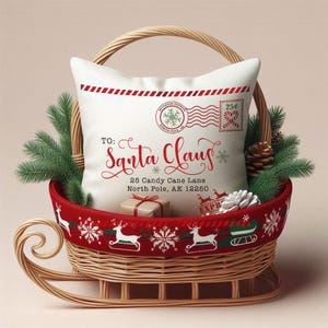 May include: A decorative Christmas pillow with a festive design, featuring the text "TO: Santa Claus" and a vintage postage stamp motif. The pillow is nestled in a wicker sleigh basket with a red trim adorned with reindeer and snowflakes.