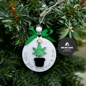 May include: A round wooden Christmas ornament with a green marijuana leaf design and the text "Hope your Christmas is dope".