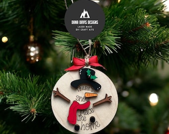 Puede incluir: Adorno de Navidad de madera con forma de muñeco de nieve con el texto "There's snow place like home". El muñeco de nieve lleva un sombrero negro, una bufanda roja y tiene ojos y boca negros.