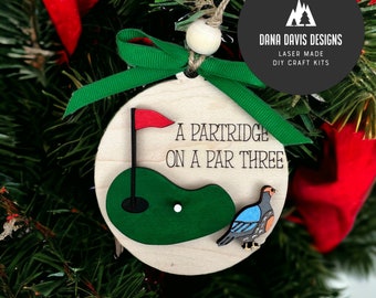 Può includere: Ornamento natalizio in legno a tema golf. L'ornamento presenta un campo da golf verde, una bandiera rossa e una pernice. Il testo sull'ornamento recita "A Partridge on a Par Three". Sono attaccati un nastro verde e una perla di legno.