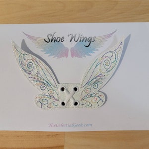 May include: White shoe wings with iridescent accents and decorative stitching. The wings are attached to a white base with four eyelets for lacing. The text "Shoe Wings" and "TheCelestialGeek.com" are visible.