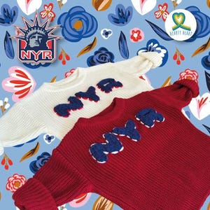 May include: Two long-sleeved knit sweaters, one white and one dark red, each featuring the letters NYR in dark blue textured applique on the chest. The sweaters have a ribbed texture and crew necklines, displayed against a blue floral background.