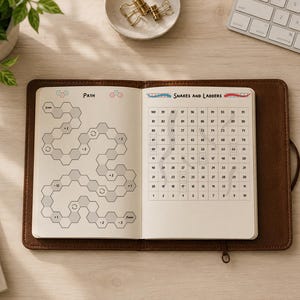 May include: An open notebook with a brown leather cover featuring two game boards on its pages. The left page shows a hexagonal path labeled Path with numerical modifiers. The right page displays a grid numbered 1 to 100 titled Snakes and Ladders.
