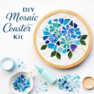 May include: DIY mosaic coaster kit with a floral design. The coaster features blue, turquoise, and white mosaic tiles arranged in a flower pattern, set within a wooden frame. Includes glue, glass pieces, and a seashell-shaped dish.