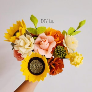 May include: A colorful DIY kit featuring a bouquet of felt flowers. The bouquet includes sunflowers, roses, and other flower types in shades of yellow, orange, and pink, with green leaves. The text "DIY kit" is visible.