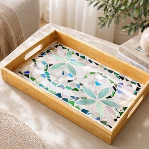 May include: A rectangular wooden serving tray with mosaic tile inlay. The mosaic features a floral design in shades of blue, green, and white. The tray has cut-out handles on each side.