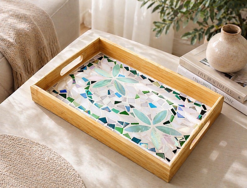 May include: A rectangular wooden serving tray with mosaic tile inlay. The mosaic features a floral design in shades of blue, green, and white. The tray has cut-out handles on each side.