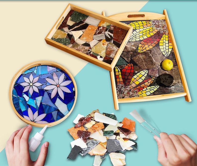 May include: Wooden serving trays with mosaic tile designs. One rectangular tray features a mosaic of colorful stone pieces. Another rectangular tray has a leaf-like mosaic. A round tray displays a blue floral mosaic.