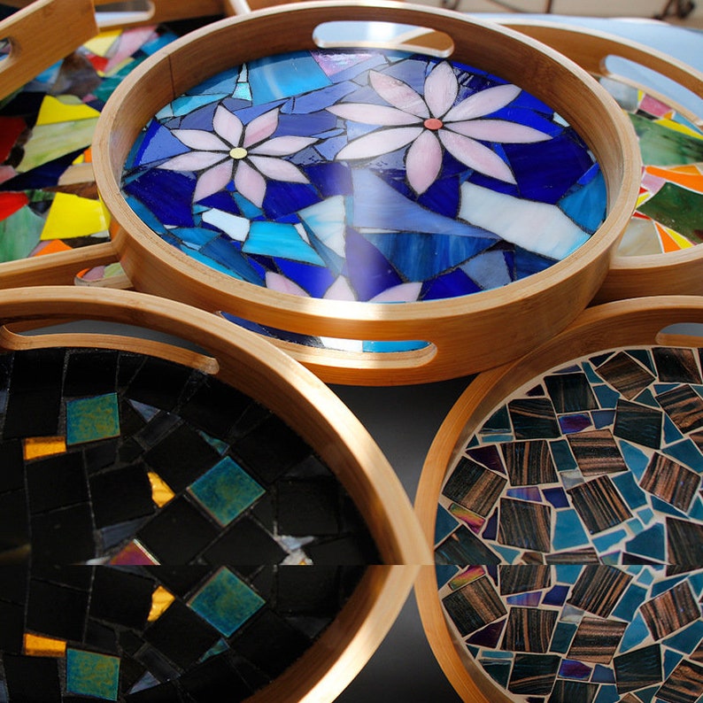 May include: A collection of round wooden serving trays with mosaic tile designs. The trays feature various mosaic patterns, including floral and abstract designs in shades of blue, black, and brown. The wooden rims have built-in handles.