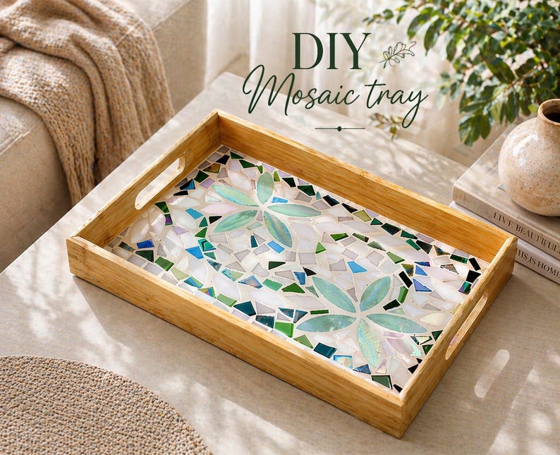 May include: A rectangular wooden tray with a mosaic tile design. The mosaic features a floral pattern in shades of green, blue, and white. The tray has cut-out handles and the text "DIY Mosaic tray" in green script.