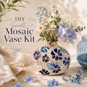 Puede incluir: Un jarrón de mosaico redondo decorado con piezas de vidrio azules y blancas en un patrón floral, lleno de un ramo de flores azules y blancas. El texto DIY Small Mosaic Vase Kit está impreso en azul oscuro y dorado en el lado izquierdo.