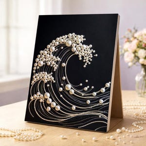 May include: A black rectangular display board featuring a decorative wave design created with white pearls of varying sizes and thin silver lines. The artwork is mounted on a wooden easel stand, showcasing a detailed, textured ocean wave motif.