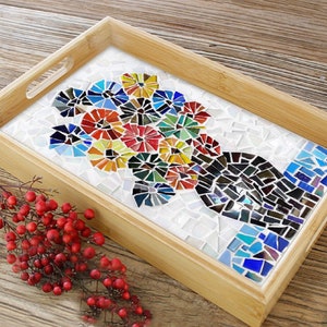 May include: A rectangular bamboo serving tray with a mosaic floral design. The mosaic features colorful flowers in shades of red, blue, yellow, and green, set against a white background. The tray has cut-out handles.