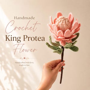 May include: A crochet King Protea flower with soft pink petals and a textured center, featuring green leaves on a brown stem. The text reads: Handmade Crochet King Protea Flower. Handcrafted with love, made to last.