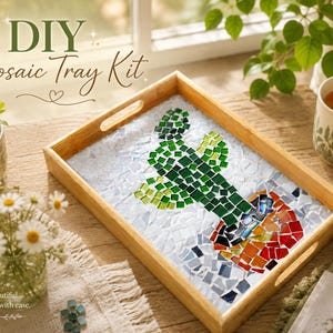 May include: A rectangular wooden tray featuring a mosaic design of a green cactus in a multi-colored pot. The background of the mosaic is composed of white tiles. The tray has cutout handles on the sides and is presented as a DIY Mosaic Tray Kit.