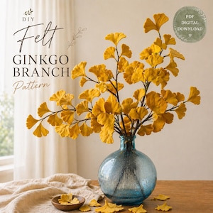 Puede incluir: Un patrón de rama de Ginkgo de fieltro DIY se muestra en un jarrón de vidrio azul. Las hojas y ramas de fieltro amarillo crean un contraste llamativo con el jarrón. La imagen incluye el texto "DIY Felt Ginkgo Branch Pattern" y una insignia de "PDF Digital Download".
