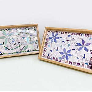 May include: Two rectangular mosaic trays with wooden frames. One tray features light green and blue floral designs, while the other showcases purple and blue flowers. Both have a mosaic tile background.