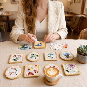 May include: A collection of mosaic coasters with floral and nature-inspired designs. The coasters are square and round, with a light wood border. A cup of coffee with latte art sits on a coaster. A person is shown crafting a coaster.
