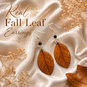 May include: A pair of drop earrings featuring preserved brown fall leaves with a glossy finish. Each earring has a silver-toned hook, a small black bead, and a clear accent bead above the leaf. The text "Real Fall Leaf Earrings" is visible.