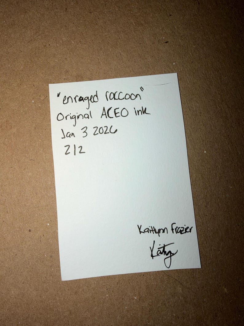Puede incluir: Una tarjeta blanca con texto manuscrito que dice "enraged raccoon" Original ACEO ink Jan 3 2020 212. La tarjeta est&aacute; firmada "Kaithlynn Frazier" con una firma debajo.
