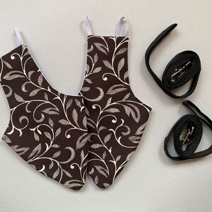 May include: Two brown and white patterned fabric pet harnesses with white straps and two black leashes with silver clasps.