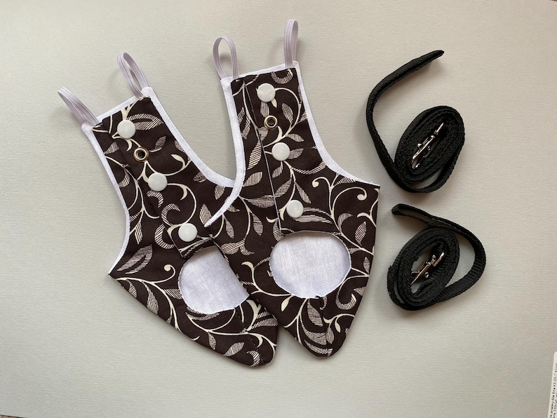 May include: Two brown and white patterned fabric dog diapers with white buttons and white trim. Two black adjustable leashes with silver clasps.