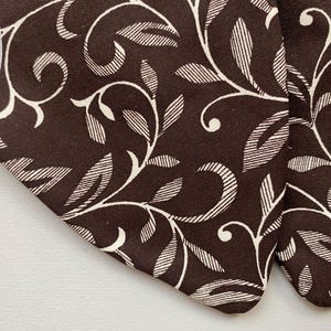 May include: Close-up of brown fabric with a white floral pattern. The fabric has a subtle texture and a repeating design of leaves and swirls.