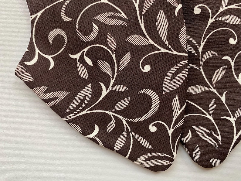 May include: Close-up of brown fabric with a white floral pattern. The fabric has a subtle texture and a repeating design of leaves and swirls.