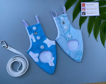 May include: Two blue pigeon pants with white accents and a matching leash. One pair features a cow print, the other a floral design. Both have snap closures and a circular opening. The leash is white with a silver clasp.