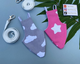 May include: Two bird flight suits, one gray with white clouds and one pink with a white star, are displayed with white leashes and metal clasps. The suits have elastic straps. The background is a light blue surface.