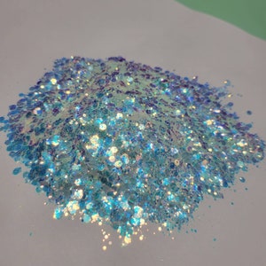 May include: A pile of iridescent blue and white glitter. The glitter is a mix of different sizes and shapes.
