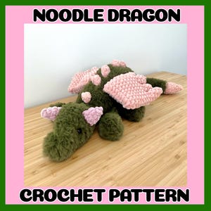 Puede incluir: Un dragón de peluche verde hecho a mano con alas y detalles rosas. El texto "NOODLE DRAGON" y "CROCHET PATTERN" se muestra en letras negras sobre un fondo rosa, enmarcado por un borde verde. El dragón está sobre una superficie de madera.