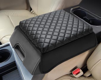 May include: A black car center console armrest cover featuring a diamond-stitched quilted pattern on the top surface. The cover has smooth black side panels with visible white stitching and a contoured shape designed to fit over a vehicle console.