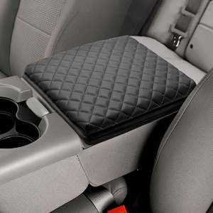 May include: Black quilted armrest cover for a car. The cover is made of a soft, padded material and has a diamond pattern.