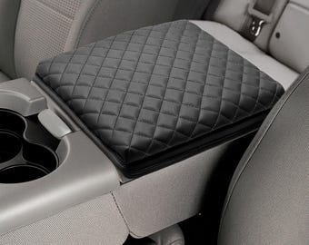 May include: Black quilted armrest cover for a car. The cover is made of a soft, padded material and has a diamond pattern.